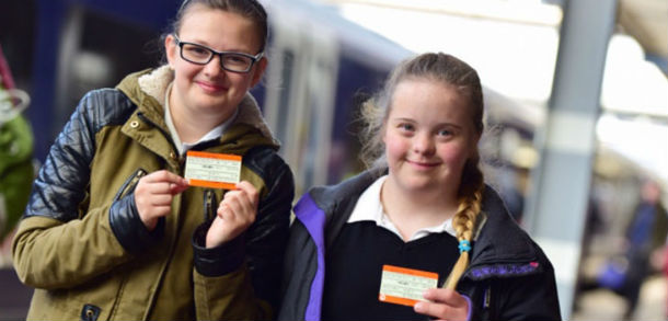 Two girls holding train tickets in front of a train at the station platform.