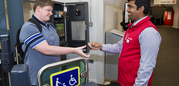 Young male showing ticket to a member of train station staff at ticket barrier